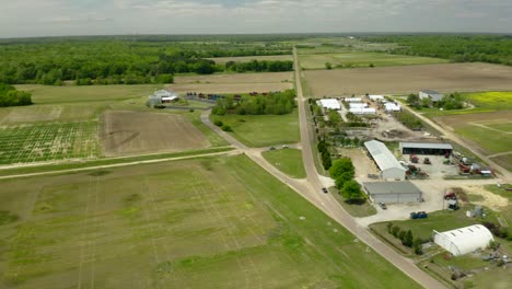 4K-Aerial-View-of-Car-Driving-down-a-Farm-Road-with-Agricultural-Buildings