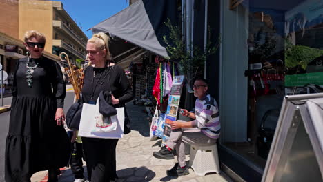 View-of-women-walking-and-man-smoking-cigarette-in-street-roads-full-of-souvenir-retail-shopping-stores-old-town-of-Kalambaka-Meteora-Trikala-Greece-Europe-travel-tourism