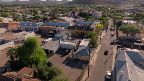 Flying-Over-Downtown-Arizona-Barrio-District-in-Daytime,-Sunny-Bright-Day-with-Cars-Driving-Towards-Mountain