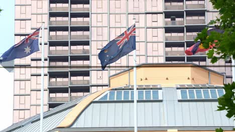 Flags-of-Australia,-Victoria,-and-the-Australian-Aboriginal-community-wave-against-downtown-buildings