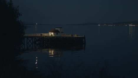 Una-Tranquila-Vista-Vespertina-De-Un-Antiguo-Muelle-Victoriano,-Con-Su-Estructura-Reflejada-En-Aguas-Tranquilas,-Con-Luces-Distantes-De-La-Ciudad-Y-Un-Cielo-Que-Se-Oscurece.