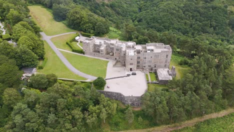 Drone-establishment-shot-of-Castle-Drogo-with-surrounding-greenery-in-Devon,-UK,-July-2024