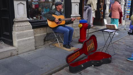 Músico-Callejero-Tocando-La-Guitarra-Y-Moviendo-Los-Pies-En-La-Ciudad-De-Quebec,-Canadá