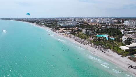 Das-Bild-Ist-Eine-Luftaufnahme-Eines-Strandes-Mit-Kristallklarem-Wasser-Eines-Hotels-In-Mahdia,-Wo-Die-Menschen-Verschiedene-Aktivitäten-Genießen