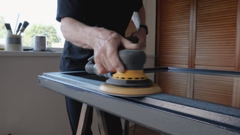 An-older-man-sands-a-window-frame-with-a-sander-for-painting