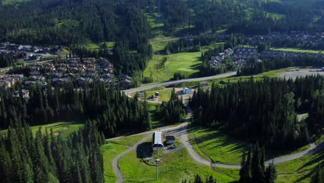 Drone-flying-down-mountain-slope-with-holiday-resort-in-Canadian-summer