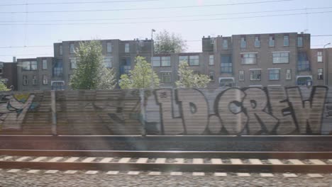 Vista-Urbana-De-Edificios-De-La-Ciudad,-Ferrocarril-Y-Grafitis-Desde-La-Ventana-Del-Tren-Que-Pasa