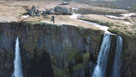 Isländisches-Hochland,-Luftaufnahme-Eines-Männlichen-Entdeckers-Auf-Majestätischen-Wasserfällen-In-Der-Landschaft-Des-Ländlichen-Islands