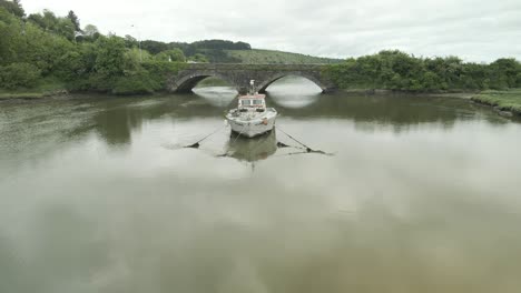 Ein-Altes-Boot-Liegt-Verlassen-Im-Fluss-In-Der-Nähe-Einer-Steinbrücke-In-Youghal,-County-Cork,-Irland