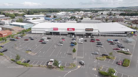 Aerial-fly-in-of-retail-park-in-Bridgwater,-displaying-various-shops,-large-parking-areas,-and-surrounding-infrastructure,-Bridgwater,-United-Kingdom,-July-2024