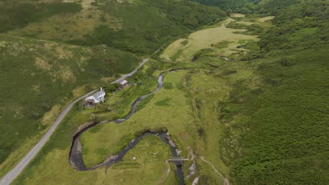 Drone-fly-in-view-of-a-remote-holiday-cottage-in-rural-countryside,-surrounded-by-lush-green-fields-and-natural-beauty