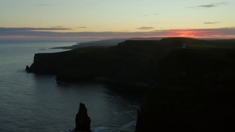 Aerial-rising-shot-above-the-Cliffs-of-Moher,-silhouetted-against-the-rising-sun