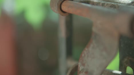 Close-up-of-a-rusty-metal-latch-on-a-green-blurred-background-in-soft-sunlight