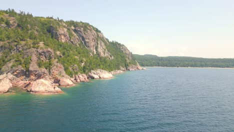 Aerial-drone-footage-of-rocky-coastal-cliffs-with-clear-blue-waters-and-lush-greenery