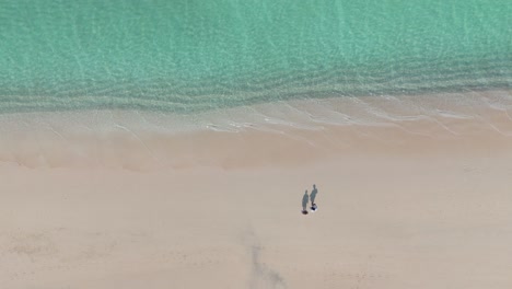 Couple-walks-towards-pristine-turquoise-sea-of-Socotra-Shoah-Beach-aerial-drone-view,-isolated-archipelago