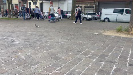 Crowded-Brussels-market-with-diverse-people-and-strollers,-cars-parked-in-background