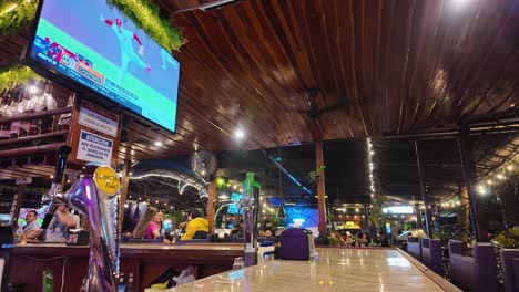 Abendlicher-Blick-Auf-Einen-Lebhaften-Pub-Von-Der-Getränketheke-Mit-Live-Sportkanälen,-Zapfhahn-Und-Menschen-Im-Hintergrund-In-Quepos,-Costa-Rica