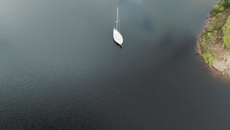 A-small-white-sailboat-viewed-from-above-by-a-drone,-anchored-in-a-lake