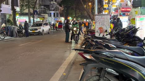 Ciclomotores-Scooter-Pasando-Ciclomotores-Estacionados-En-Fila-En-Hanoi,-Vietnam