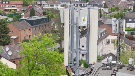 4G-telecom-communication-cell-mast-mounted-on-residential-property-in-German-neighborhood,-drone-pull-back-shot