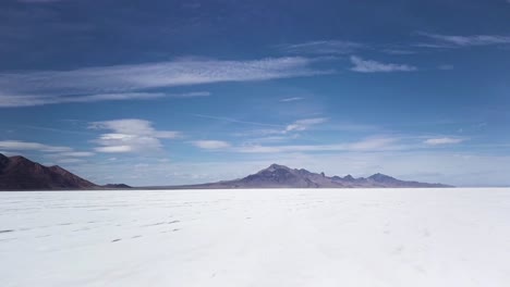 Schneller-Drohnenflug-über-Die-Bonneville-Salt-Flats-Mit-Bergen-In-Der-Ferne-Und-Blauem-Himmel-Am-Horizont