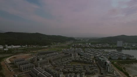 Aerial-shot-of-urban-development-near-green-hills-and-open-landscape-at-dusk