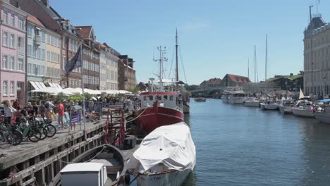 La-Calle-Nyhaven-De-Copenhague-Está-Repleta-De-Turistas,-Con-Barcos-Y-Veleros-En-Primer-Plano.