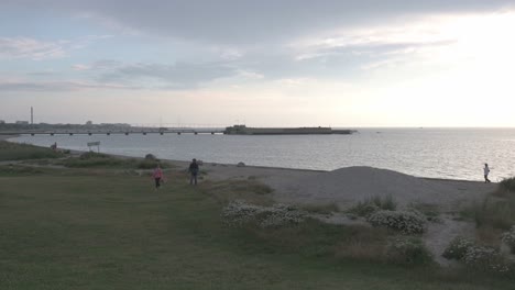 Playa-De-Copenhague-Durante-La-Puesta-De-Sol,-Con-Gente-Caminando,-Algunos-Pasean-A-Sus-Perros