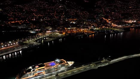 Aerial-View-of-Cruise-Ship-in-Funchal-Port-at-Night,-Promenade-and-Buildings-in-Lights,-Madeira-Island,-Portugal