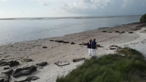 Luftaufnahme-Eines-Liebevollen-Seniorenpaares,-Das-Händchen-Haltend-Am-Strand-In-Florida-Spazieren-Geht