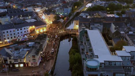 Aerial-dolly-shot-of-Galway-city-center-packed-with-spectators-during-the-Pegasus-parade-at-night