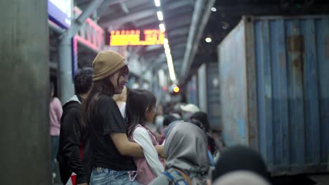 Mother-And-Daughter-Watching-A-Cargo-Train-Passes-By-The-Platform-Of-Kampung-Bandan-Station-In-North-Jakarta,-Indonesia