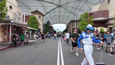 Visitantes-En-La-Concurrida-Escena-De-Una-Calle-En-Universal-Studios-Japan-Con-Tiendas-Y-Personal-De-Limpieza.