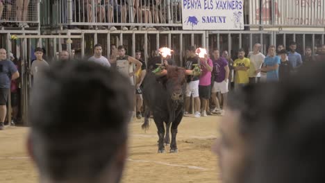 Large-bull-with-fireballs-on-its-horns-in-a-bullring-with-spectators-at-a-toro-embolado-event-in-Sagunto