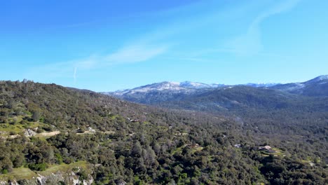 Aerial-view-of-Yosemite-National-Park,-green-forests,-rolling-hills,-snow-capped-mountains,-clear-blue-sky,-scenic-landscape,-nature's-tranquility,-USA