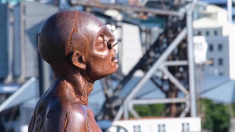 Close-up-of-iconic-solace-in-the-wind-sculpture-statue-of-man-overlooking-harbour-and-capital-city-of-Wellington,-New-Zealand-Aotearoa