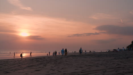 Die-Menschen-Genießen-Den-Sonnenuntergang-Am-Meer-Bei-Einem-Spaziergang-Am-Sandstrand-Von-Uluwatu---Weitwinkelaufnahme-Aus-Niedriger-Perspektive