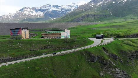 Rising-aerial-view-of-car-driving-toward-hotel-in-lush-summer-alpine-landscape