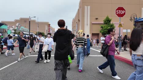 Gente-Caminando-En-Una-Concurrida-Intersección-En-Universal-Studios-Japan-Con-Tiendas-Y-Atracciones.