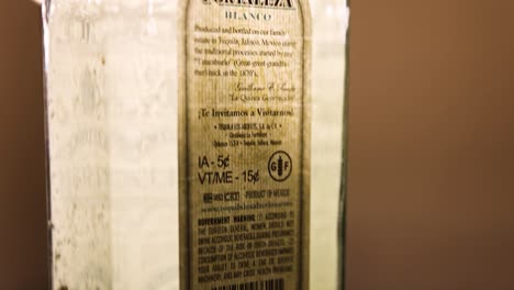 Das-Hintere-Etikett-Einer-750ml-Flasche-Fortaleza-Blanco-Tequila-Nom-1493-Wird-Von-Einer-Warmfarbigen-Lampe-Von-Hinten-Beleuchtet.-Die-Kamera-Schwenkt-Nach-Unten