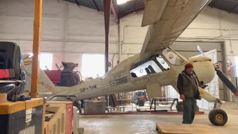 Timelapse-lateral-view-of-a-group-of-4-technicians-working-in-a-grey-color-small-airplane-inside-the-workshop