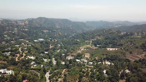 Aerial-rising-shot-of-Beverly-Hills-city-with-green-forest-mountains-on-sunny-day