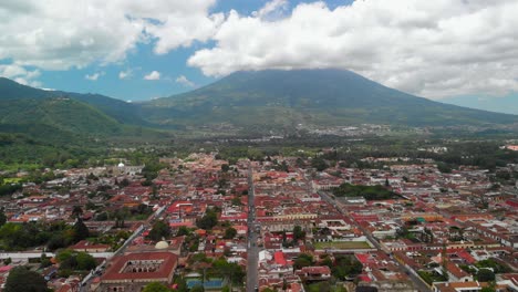 Drone-footage-showcasing-Antigua-cityscape-with-Volcano-Acatenango-towering-through-the-skies