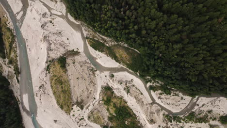 Drone-top-down-of-meandering-floodplain-river-below-evergreen-forest-with-grey-tan-sediment-deposits