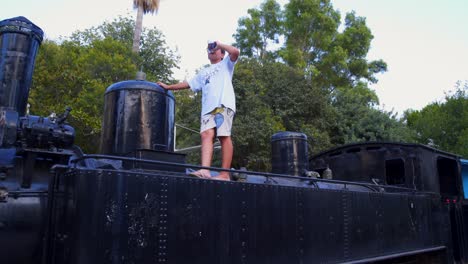 Wide-,-push-in-panoramic-footage-of-10-years-old-caucasian-boy,-walking-on-the-engine-of-an-old,-retired-locomotive-steam-train,-at-Kalamata's-railway-museum-park,-4k-29