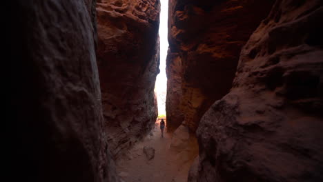 Woman-Walking-in-Narrow-Canyon-Between-Red-Sandstone-Rocks,-Slow-Motion