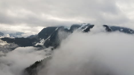 Thick-blanket-of-grey-white-clouds-reveal-evergreen-trees-and-snow-pockets-in-mountain-slope-valleys