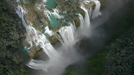 Drone-orbit-ascend-above-Tamul-waterfall,-grand-colorssal-water-cascading-into-canyon