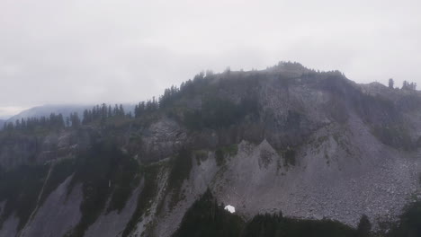 Panoramic-aerial-dolly-rises-above-rocky-boulder-field-to-forested-ridgeline-hidden-in-mist