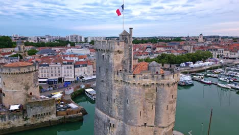 Chain-and-Saint-Nicolas-towers-with-French-flag-waving,-La-Rochelle-old-port,-France